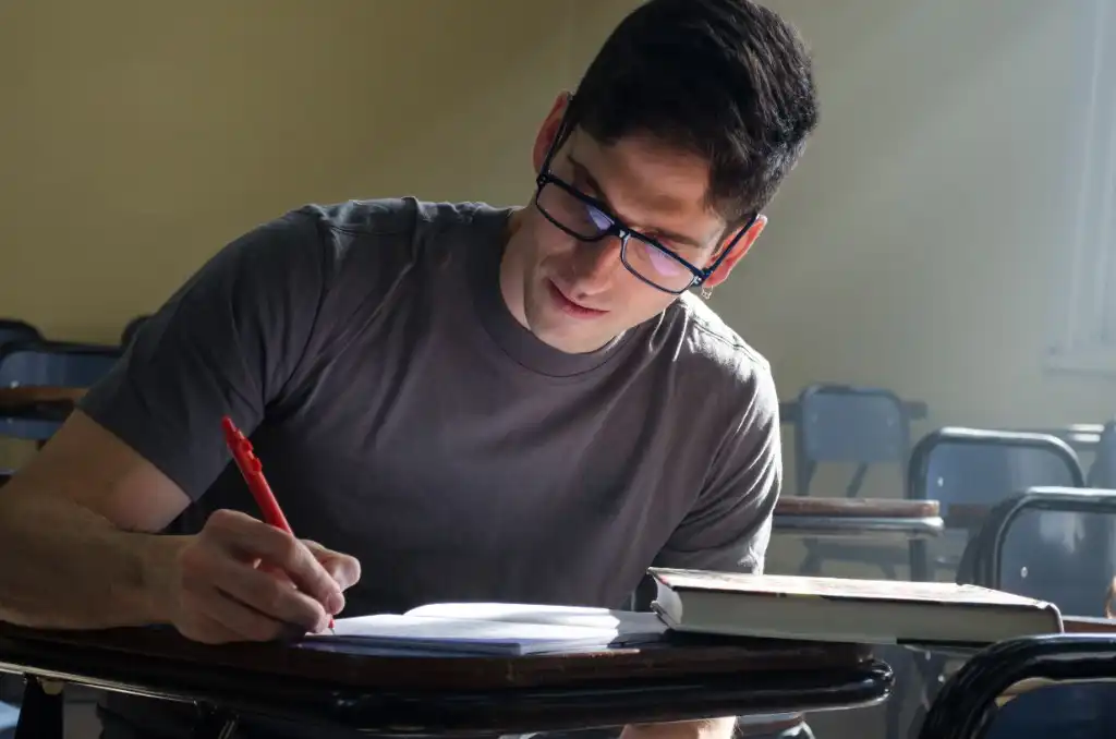 Jovem estudando e anotando em caderno em sala de aula iluminada